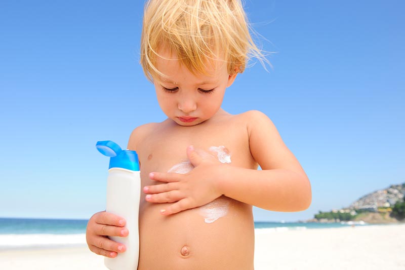 child applying sunscreen at the beach